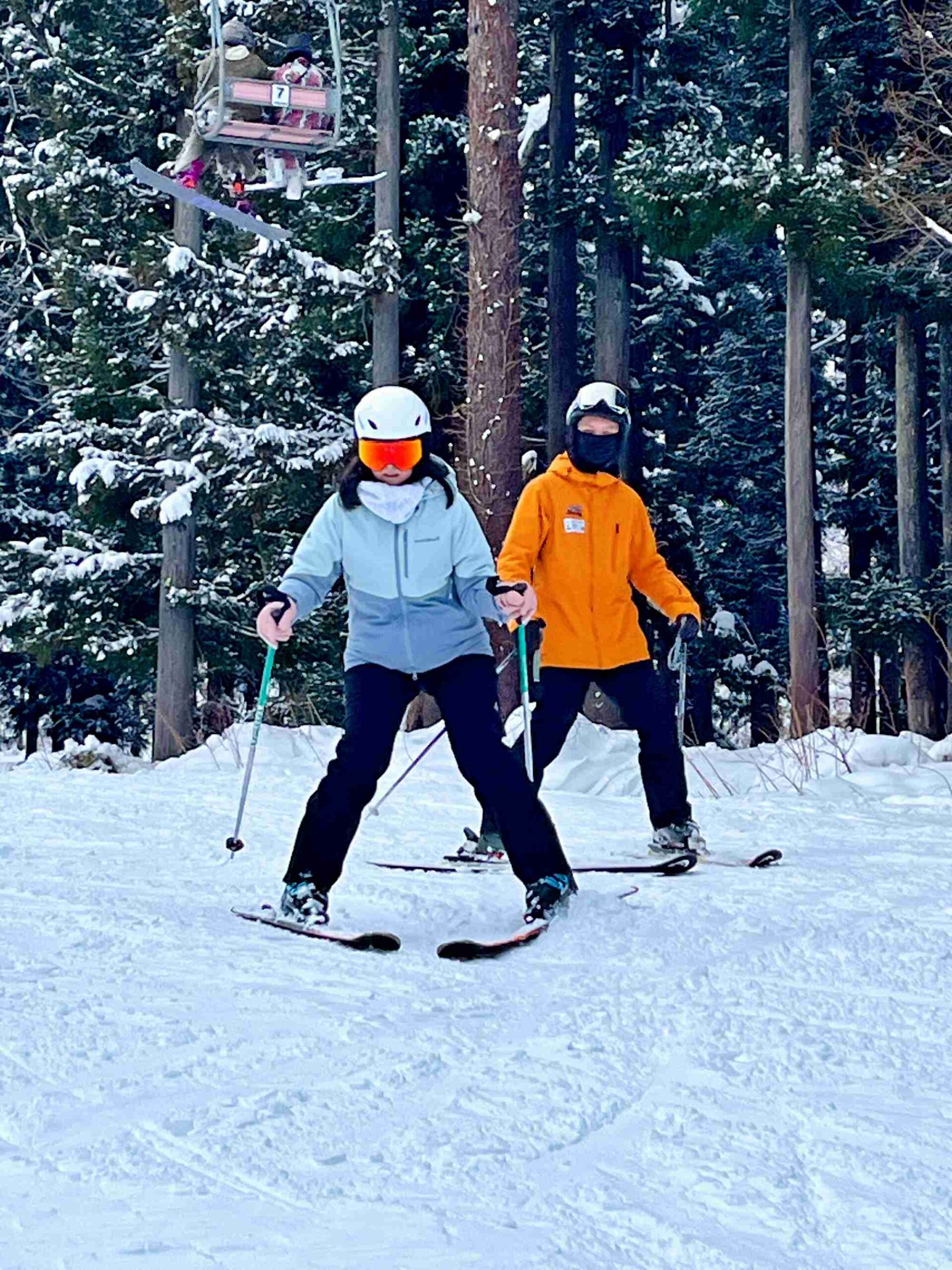 專業滑雪教練隨行一對一雪上實務教學與姿勢矯正 滑雪教練穿著橘色雪衣在學員身後進行近距離雙板(SKI)滑行姿勢與動作矯正指導